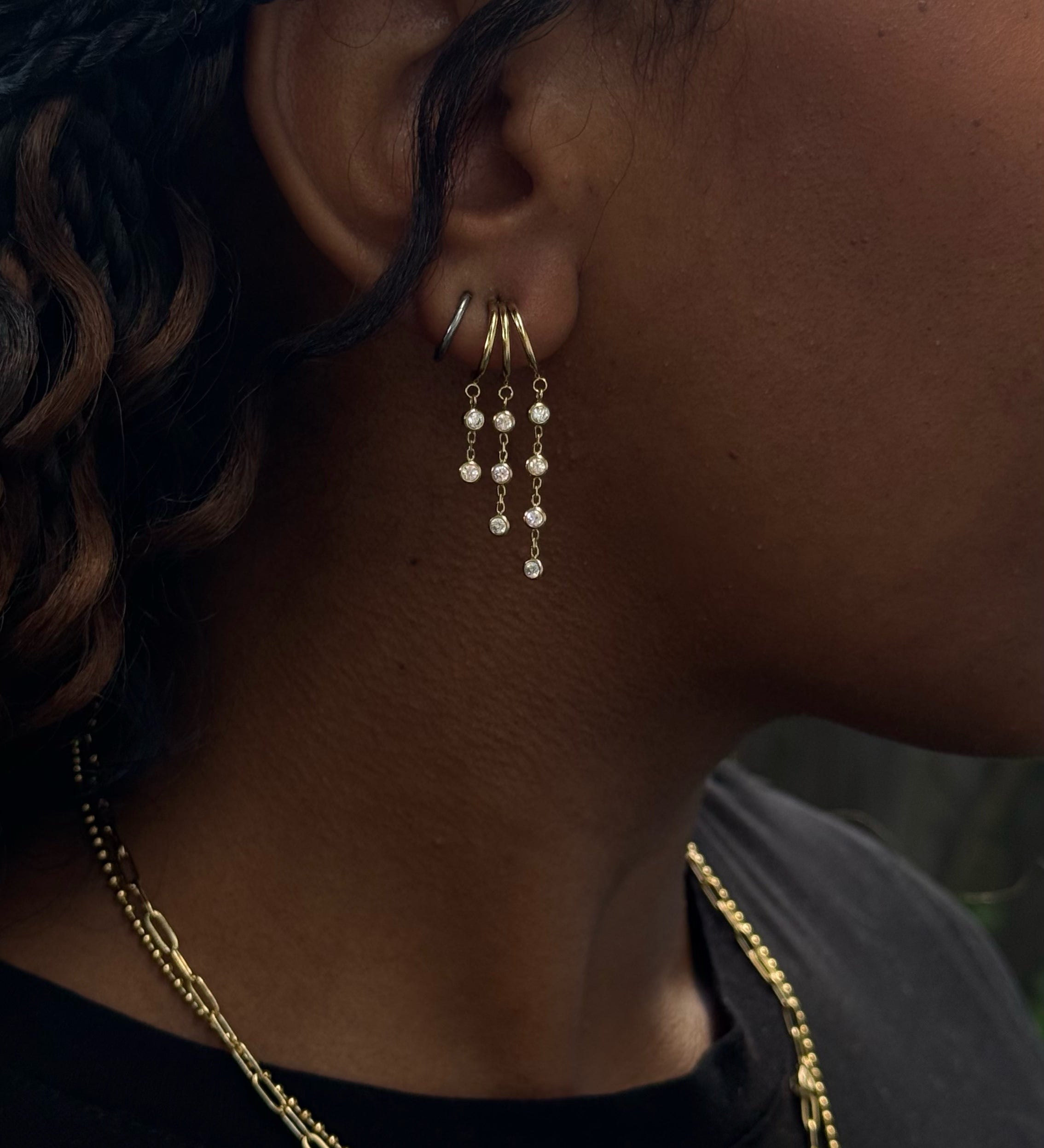Close-up side view of a woman wearing gold earrings, and necklaces in a black shirt