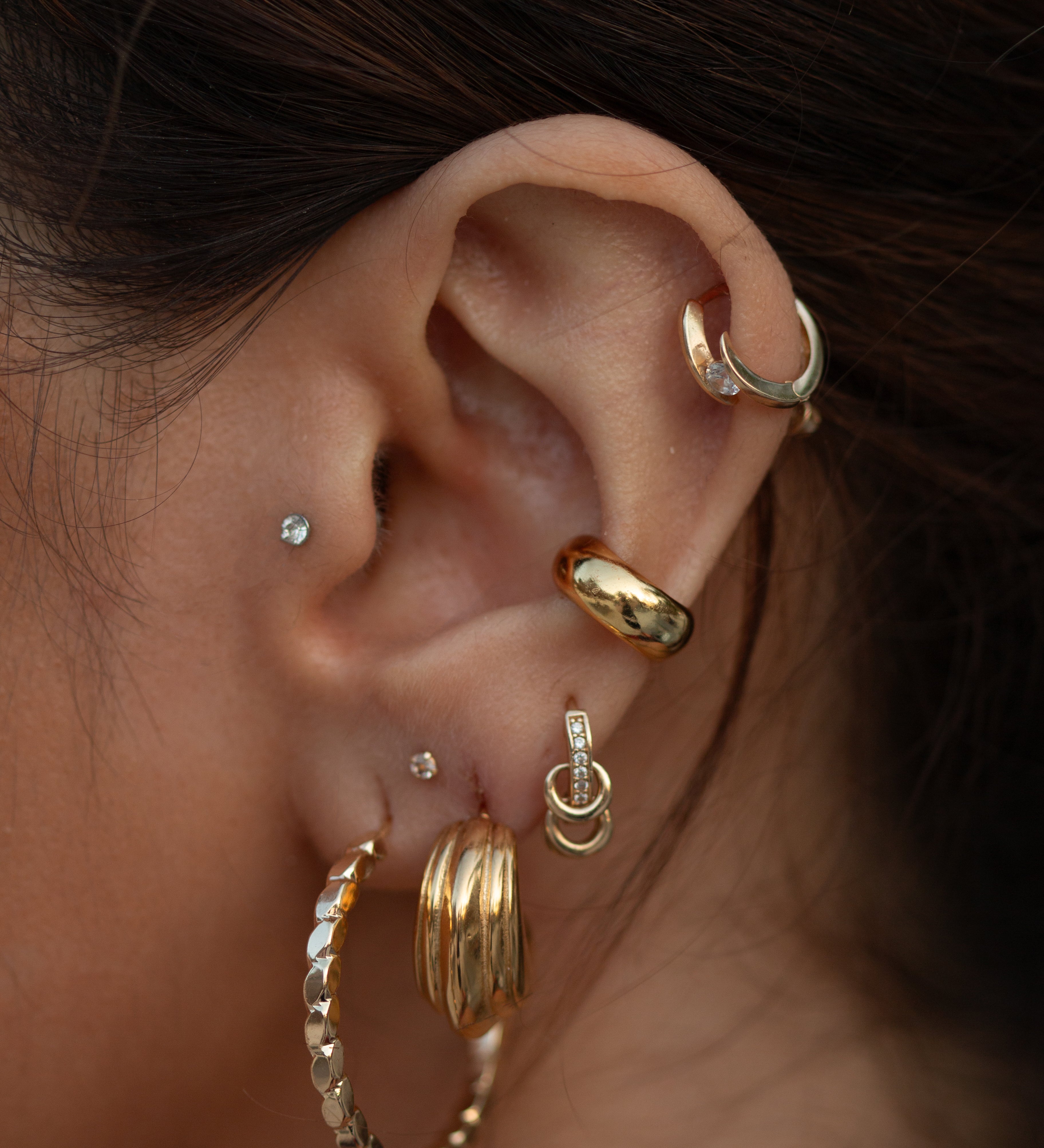 Close-up of an ear with multiple gold and crystal earrings 