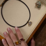 Necklace with a pendant on a display box, hand wearing a ring with a red stone.