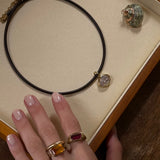 Necklace with a pendant on a display box, hand wearing a ring with a red stone.
