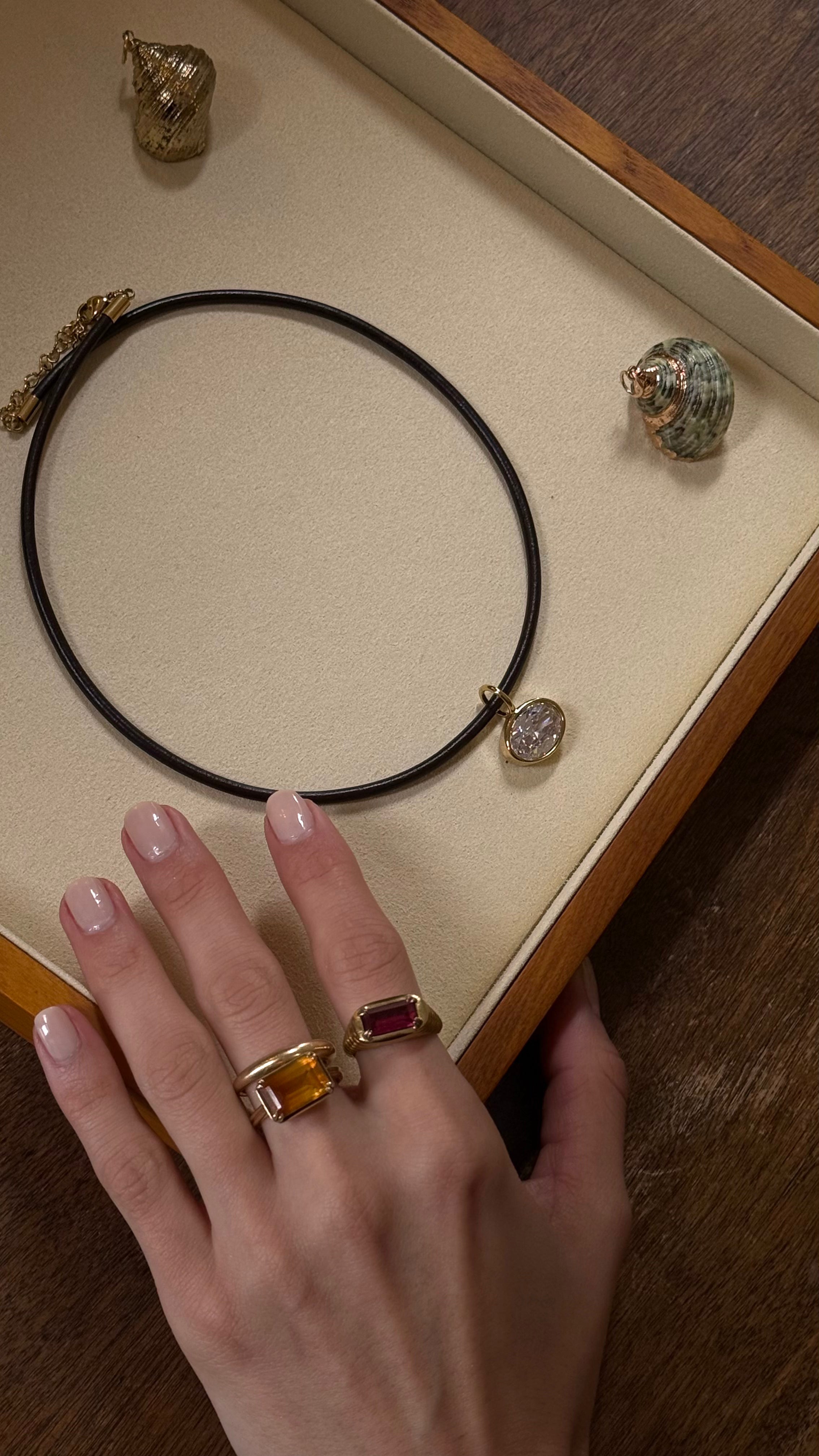 Necklace with a pendant on a display box, hand wearing a ring with a red stone.