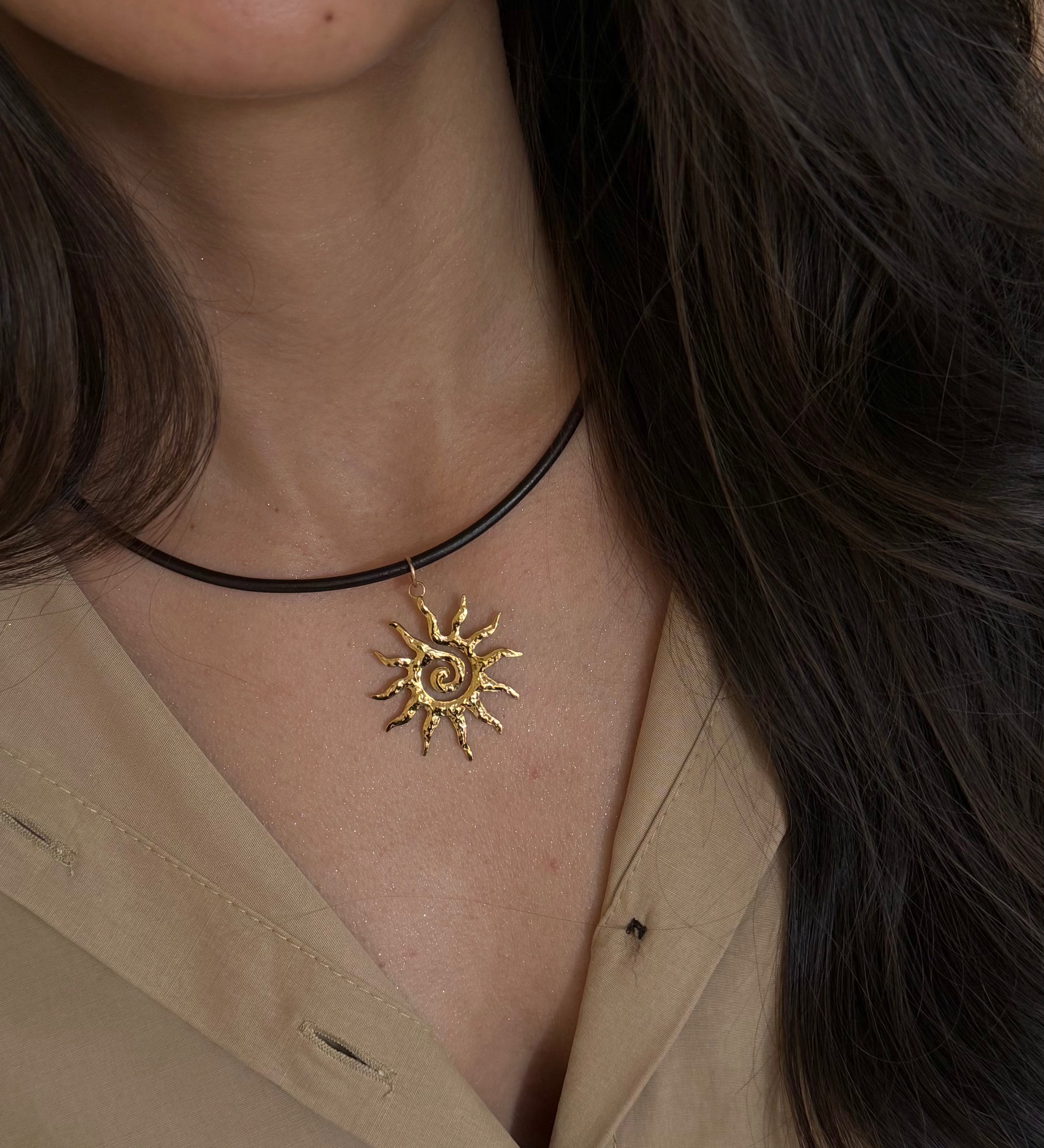 Close-up of a woman wearing a gold sun-shaped necklace on a beige background