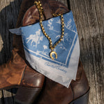 Brown cowboy boots with a blue bandana and gold necklace on a wooden surface