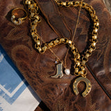 Gold chain necklace with boot and horseshoe charms on a textured brown surface