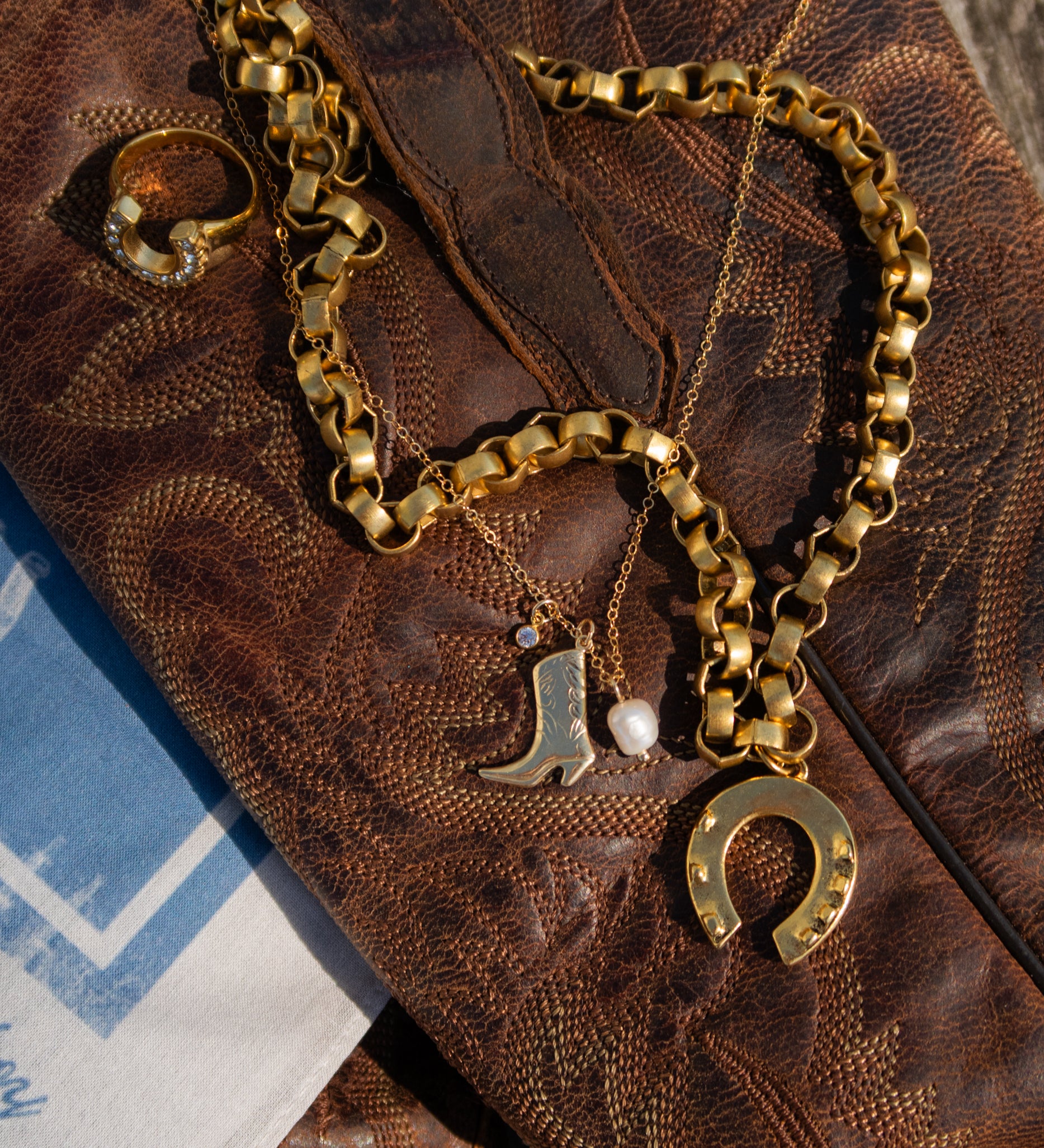 Gold chain necklace with boot and horseshoe charms on a textured brown surface