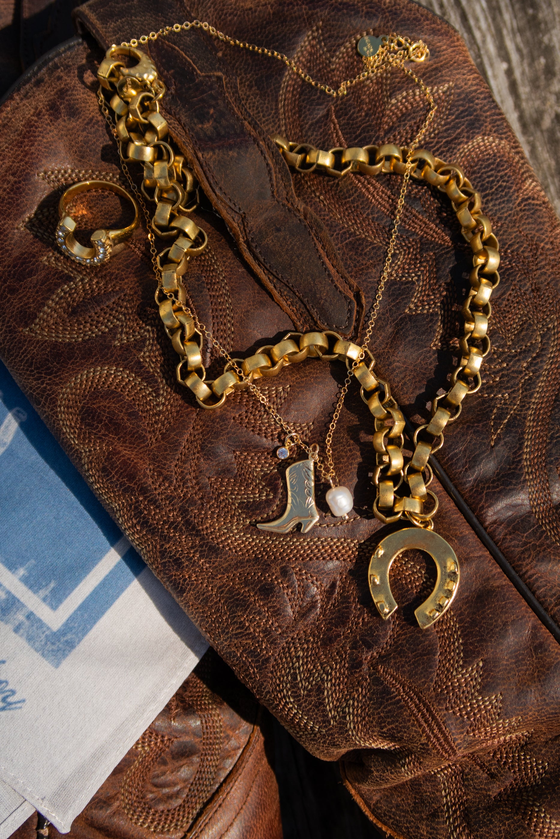 Gold chain necklace with boot and horseshoe charms on a textured brown surface