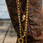 Gold chain with horse shoe charm on a brown boot with intricate patterns.