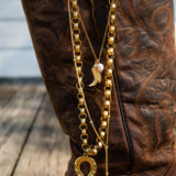 Gold chain with horse shoe charm on a brown boot with intricate patterns.