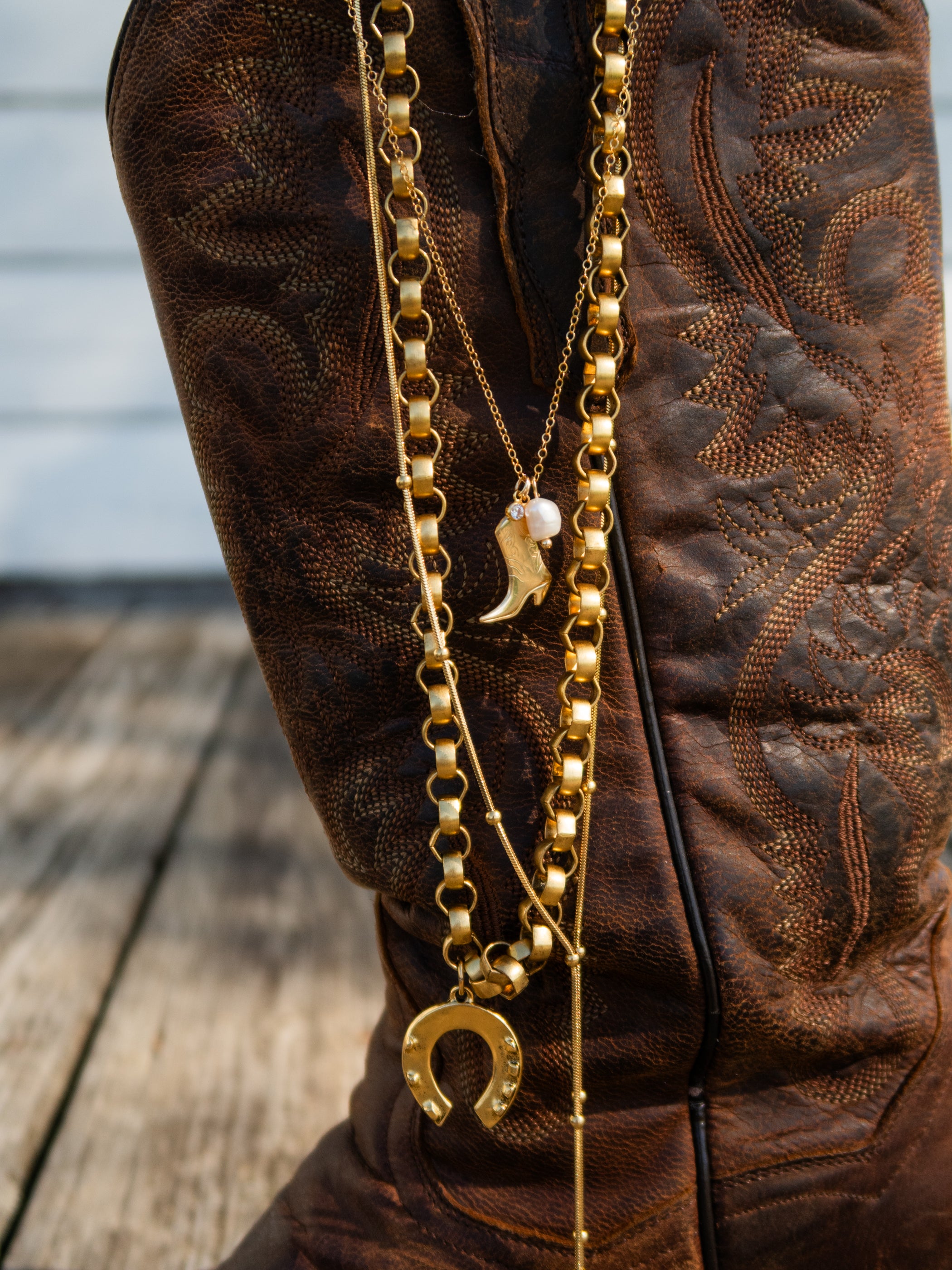 Gold chain with horse shoe charm on a brown boot with intricate patterns.