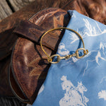 Brown leather bag with a gold ring on top of a blue fabric with white patterns.