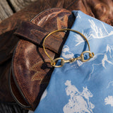 Brown leather bag with a gold ring on top of a blue fabric with white patterns.