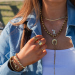 Person wearing gold jewelry including a necklace, rings, and bracelets outdoors.