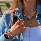Person wearing gold jewelry including a necklace, rings, and bracelets outdoors.