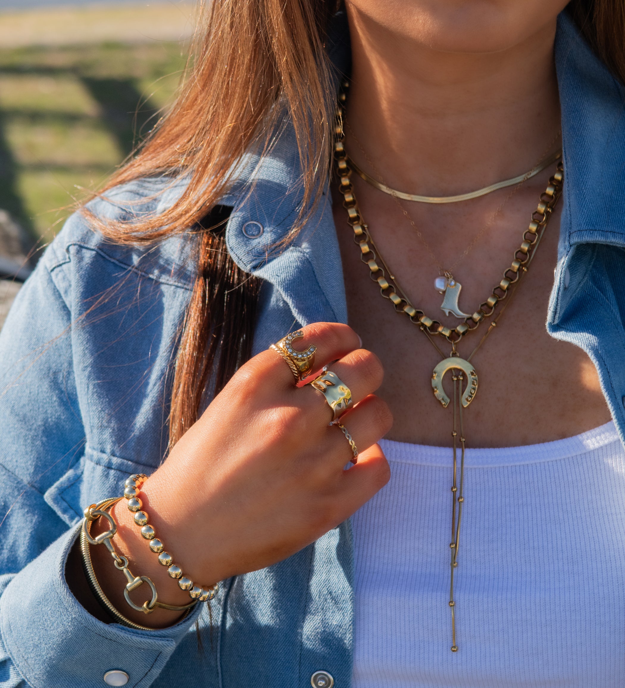 Person wearing gold jewelry including a necklace, rings, and bracelets outdoors.