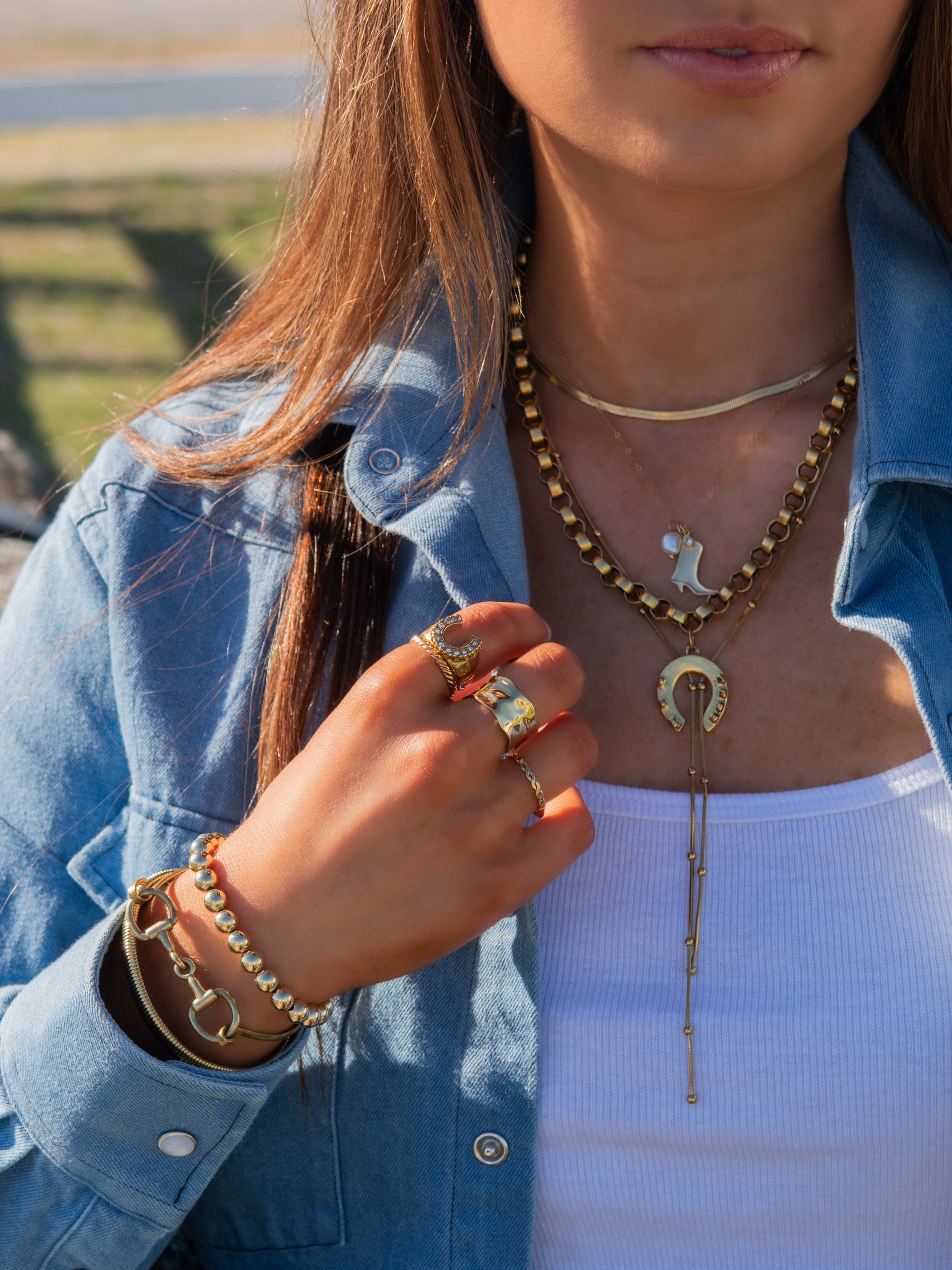 Person wearing gold jewelry including a necklace, rings, and bracelets outdoors.