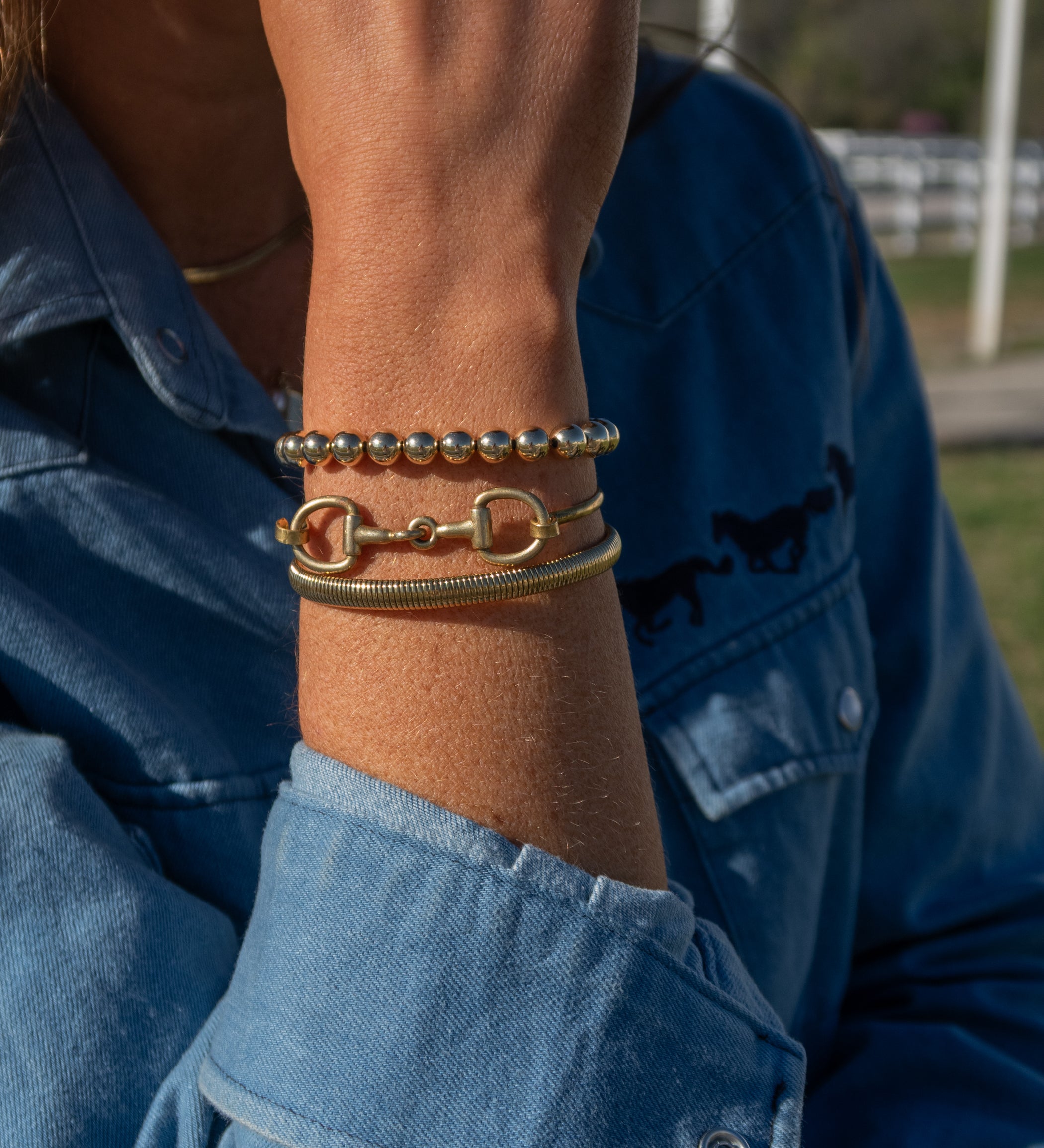 Close-up of a person's wrist wearing multiple bracelets with a blue denim jacket in the background.