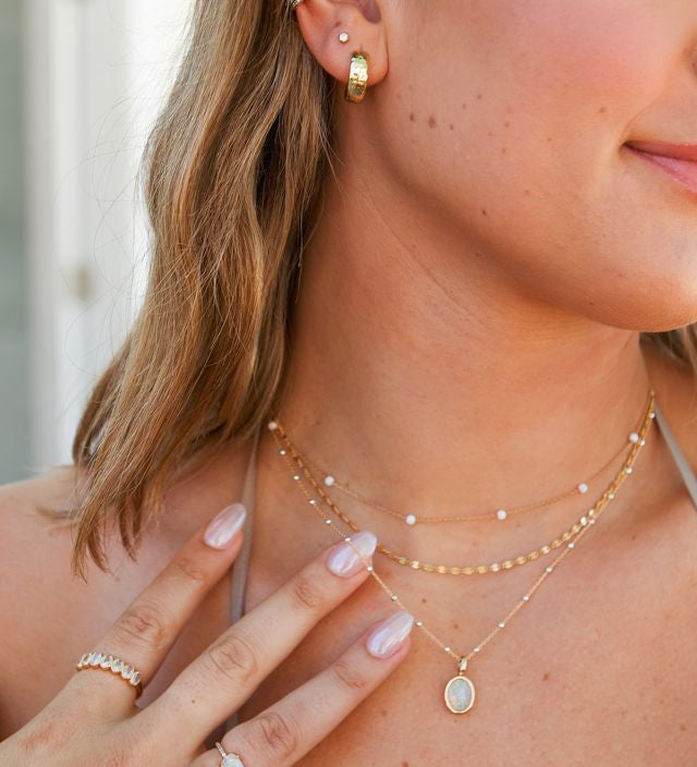 A woman wearing dainty necklaces, earrings, and rings