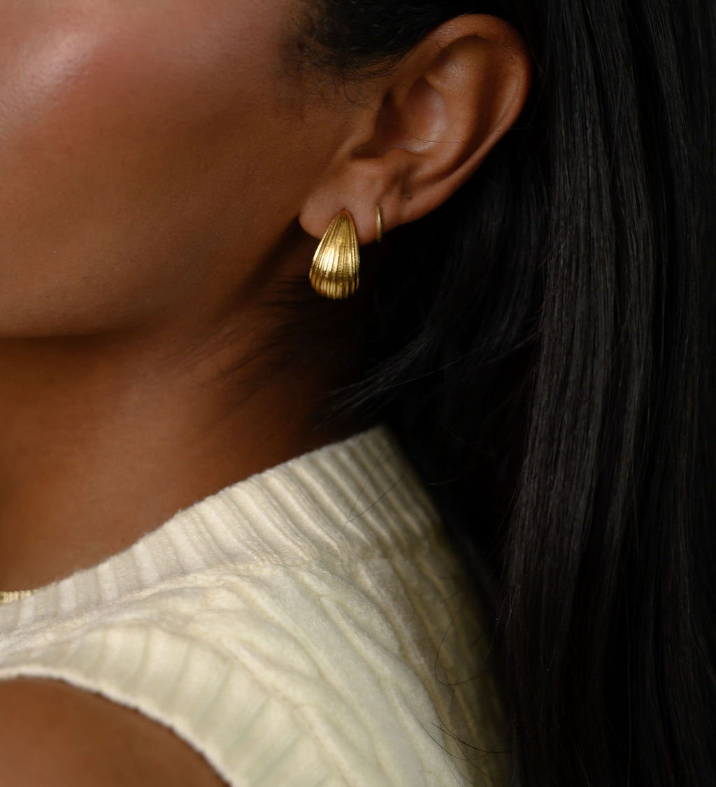 A woman wearing gold earrings and a white top