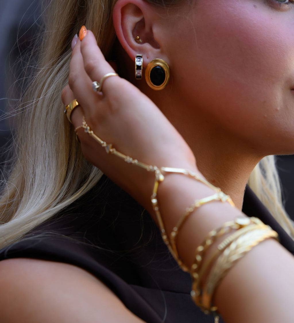 A woman wearing statement gold earrings, rings, and bracelets  