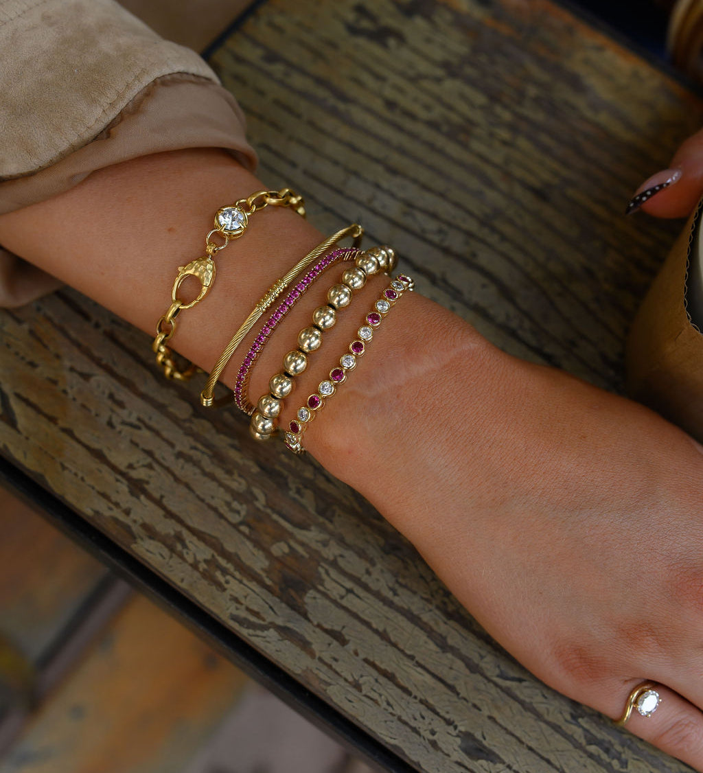 Close-up of a wrist wearing multiple gold bracelets on a textured surface