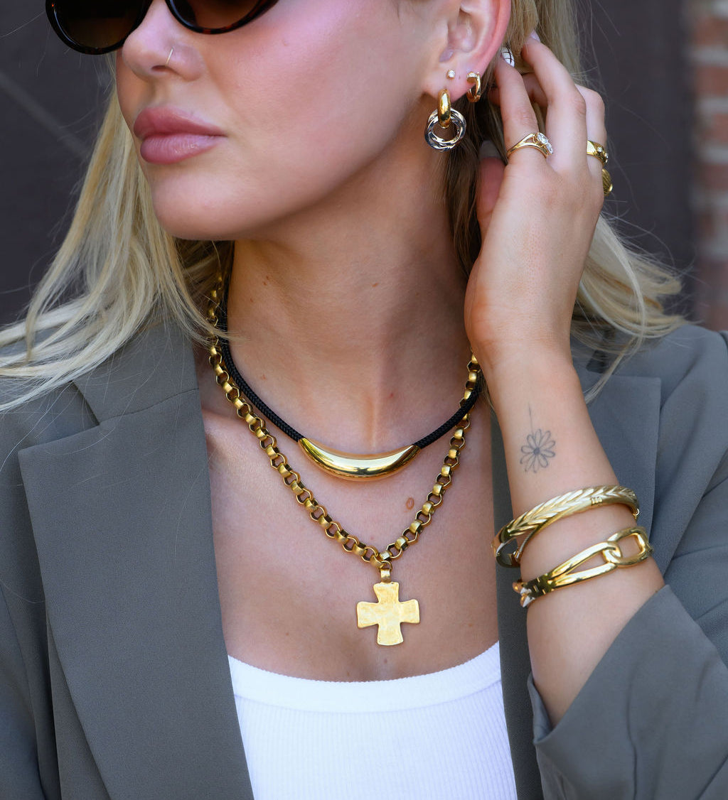 A woman wearing chic gold jewelry and sunglasses in a patterned blazer