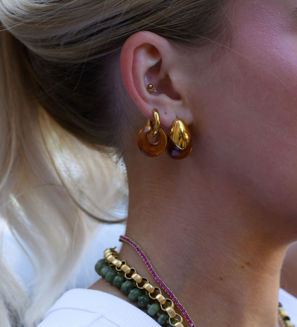 A woman wearing statement gold and stone earrings and necklaces   
