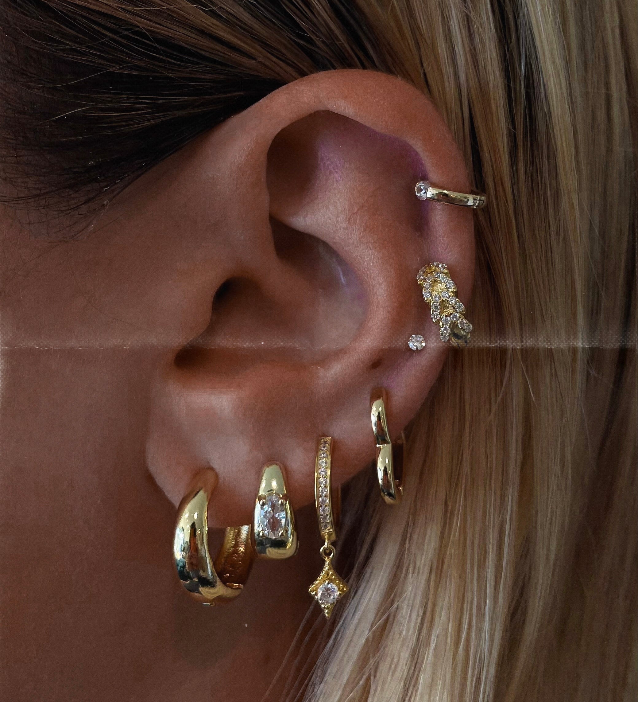 Close-up of an ear with multiple gold and crystal earrings 
