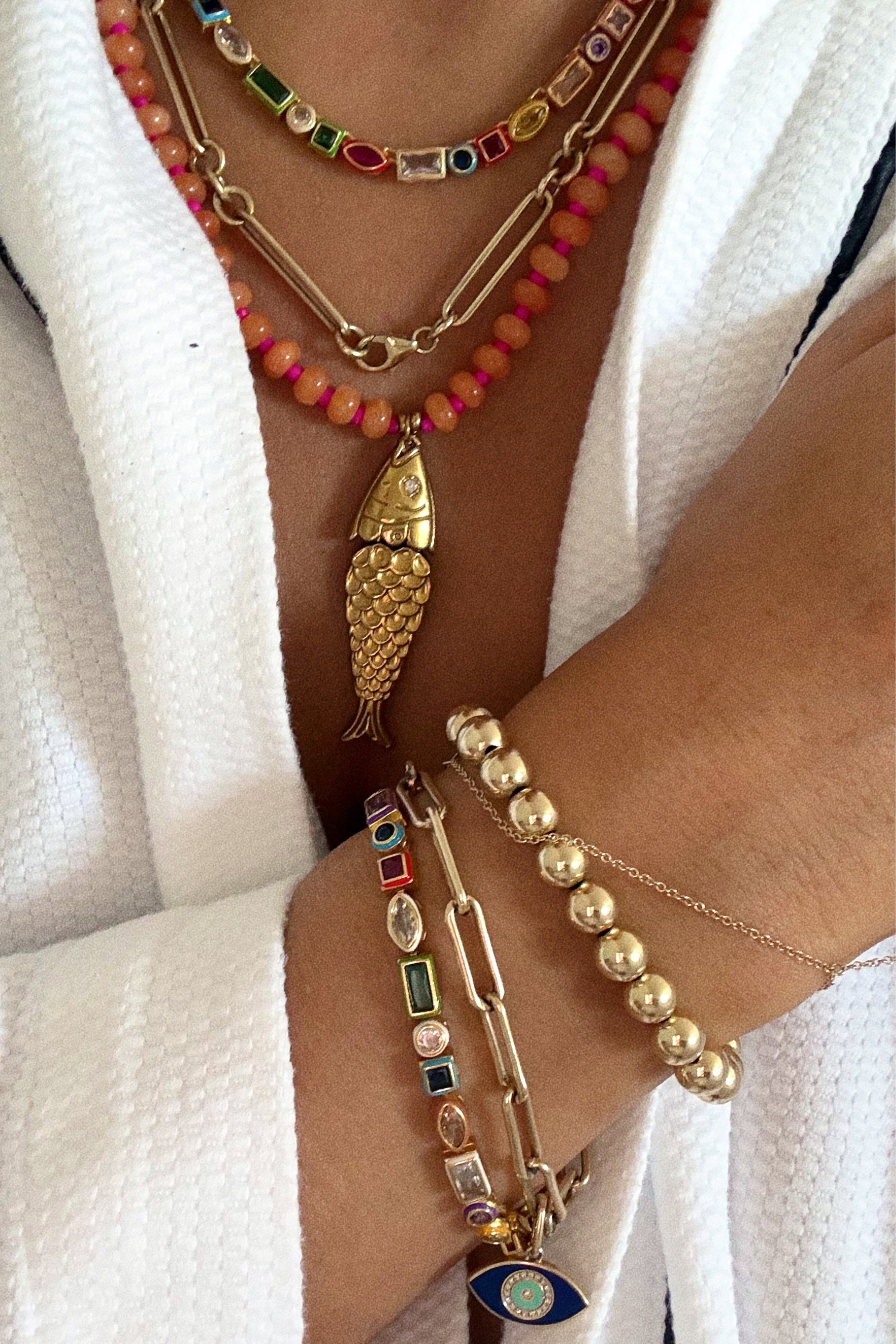 Close-up of a person wearing multiple necklaces and bracelets with colorful beads and gold accents.
