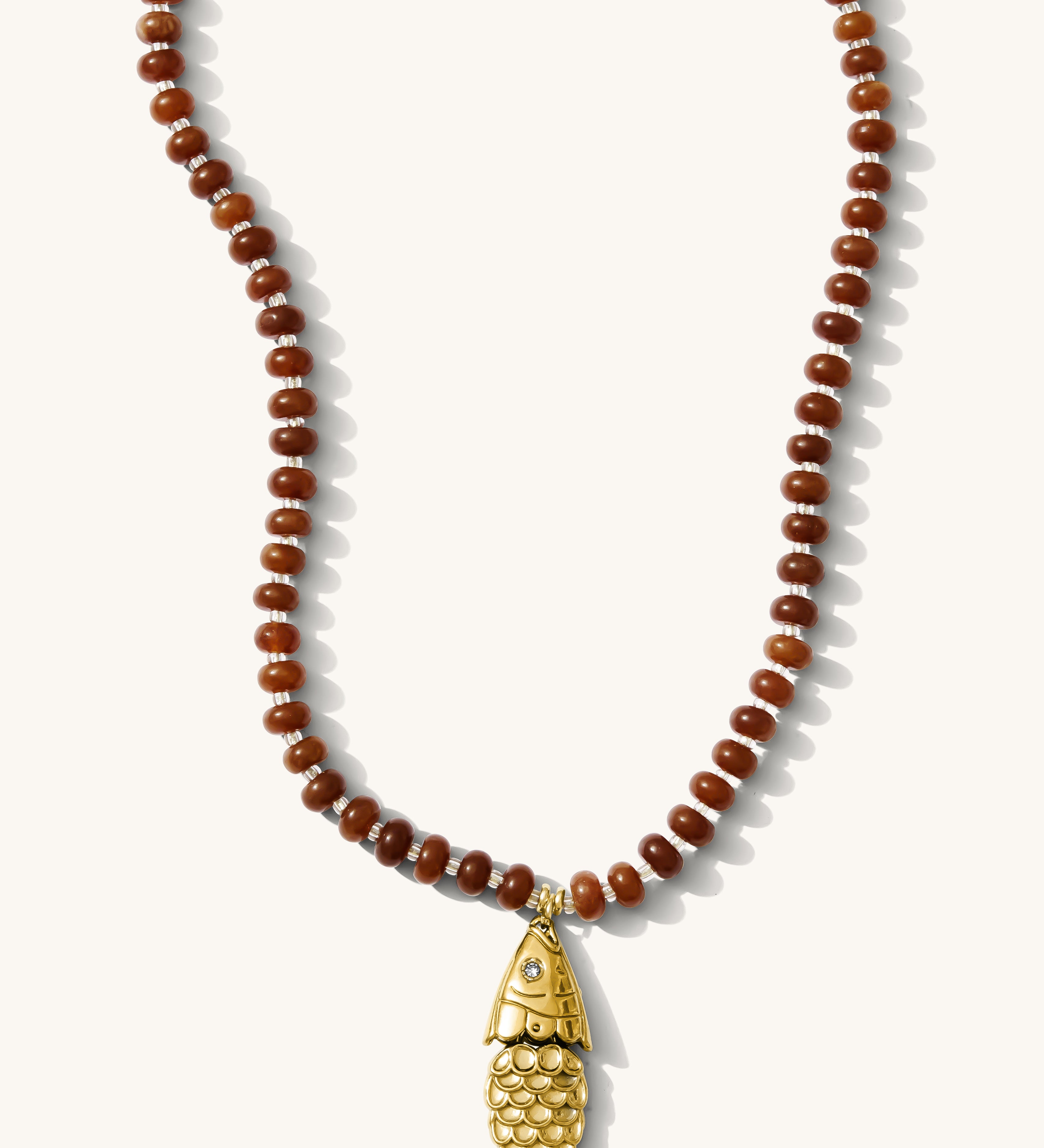 Close up of the Pez necklace in bronze gemstones with a fish charm on a white background