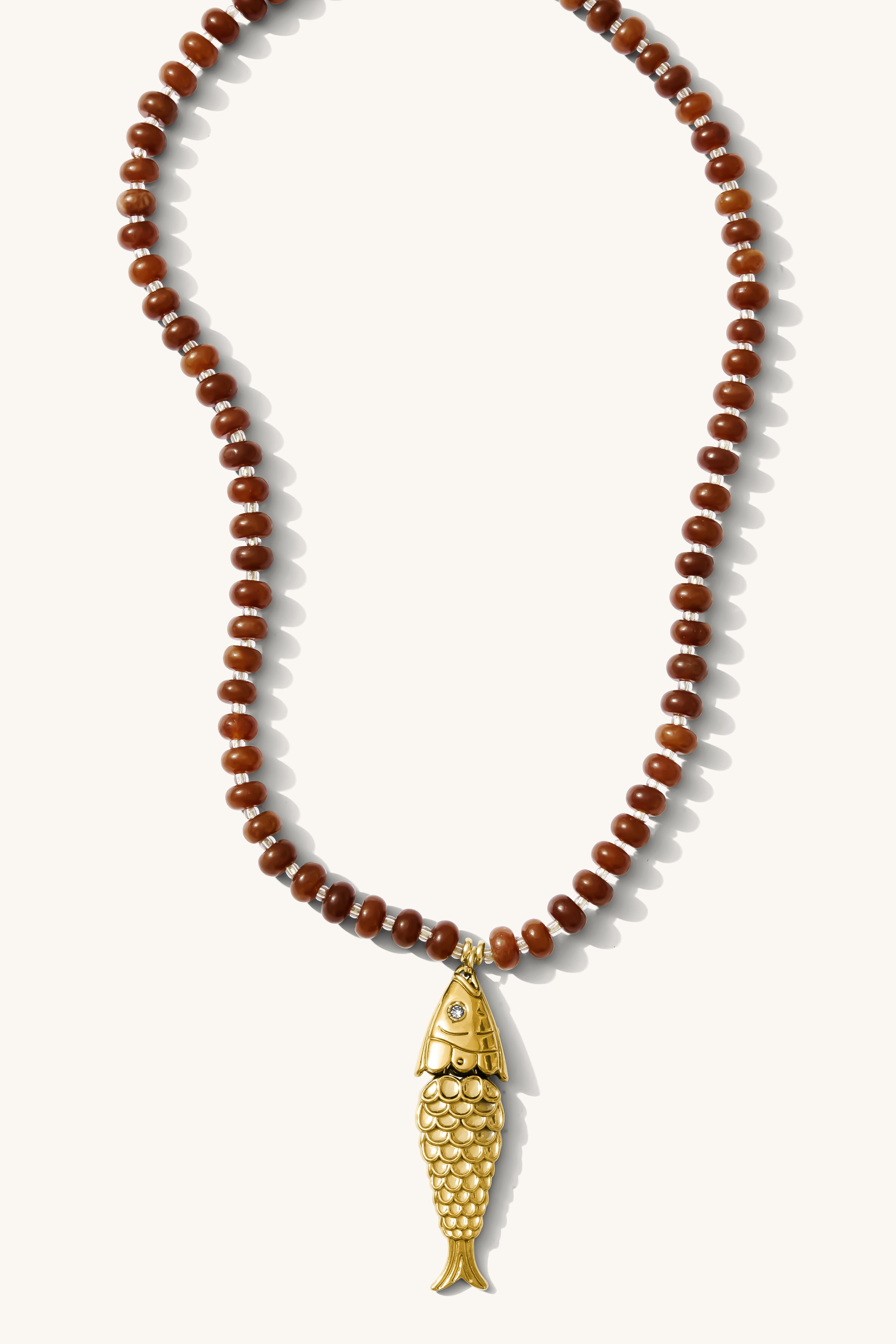 Close up of the Pez necklace in bronze gemstones with a fish charm on a white background