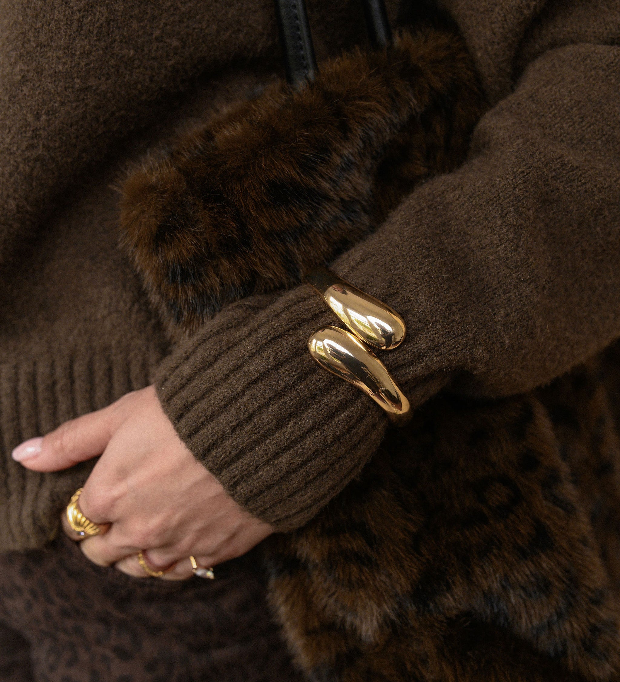 Close-up of a person wearing a brown sweater and fur bag with a gold bracelet.