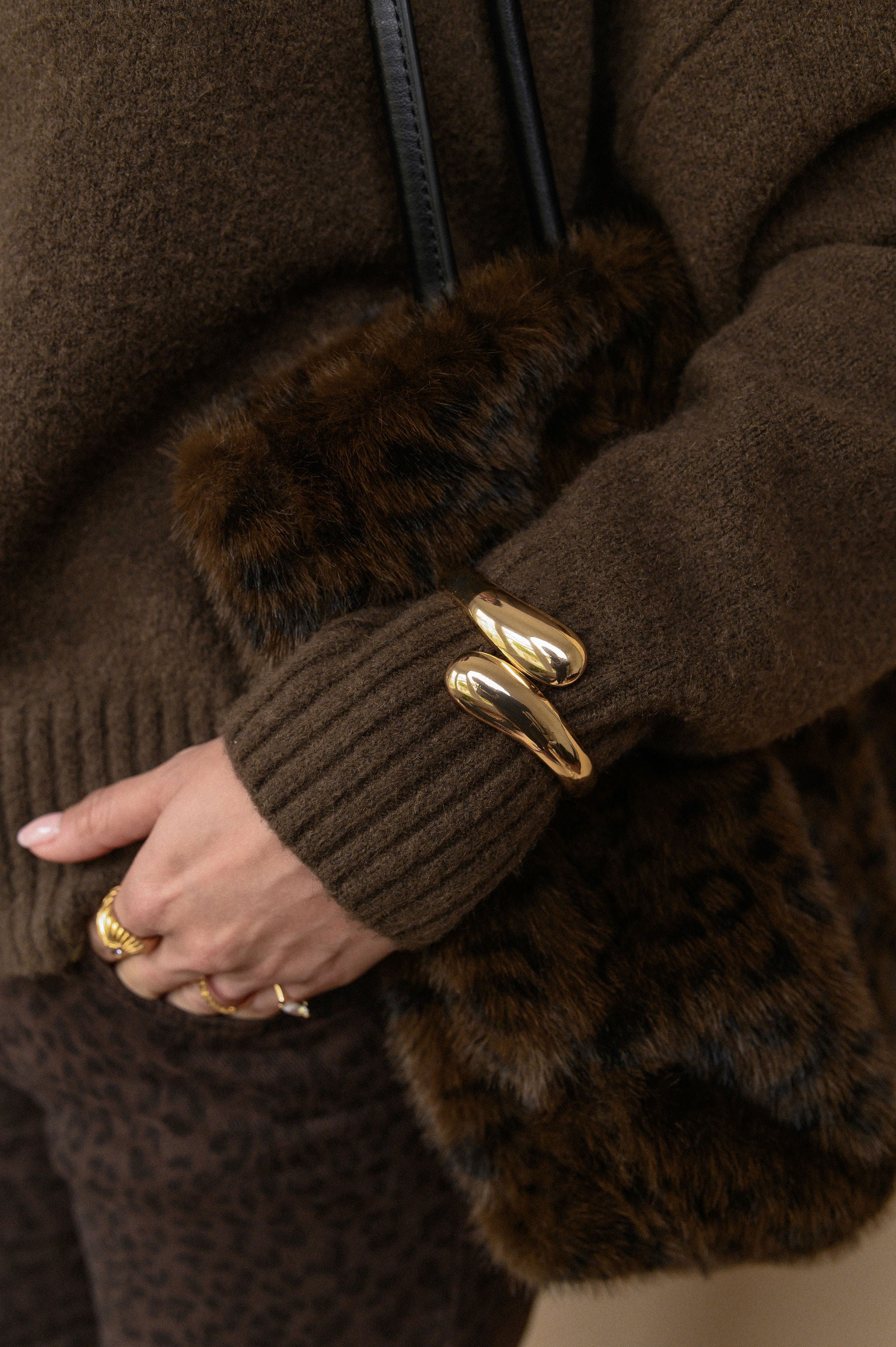 Close-up of a person wearing a brown coat with fur trim and gold bracelet.