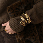 Close-up of a person wearing brown gloves with fur cuffs and gold bracelets.