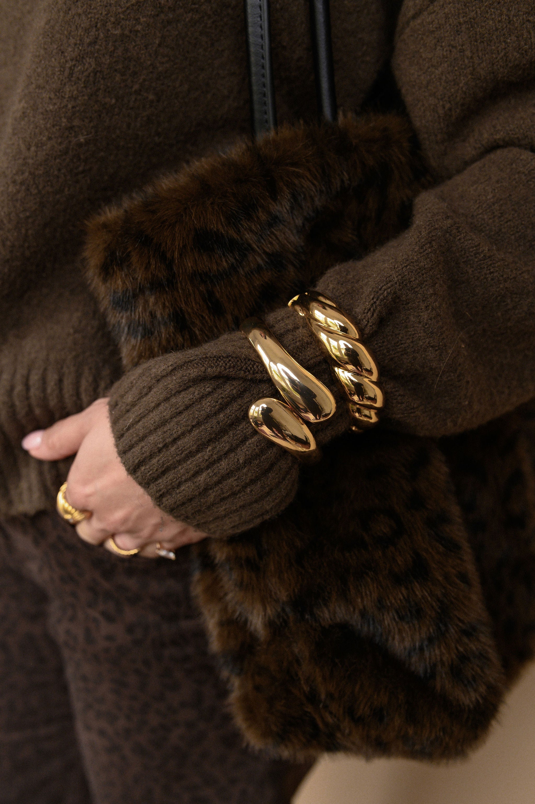 Close-up of a person wearing brown gloves with fur cuffs and gold bracelets.