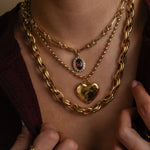 Close-up of a person wearing multiple gold necklaces with heart and chain designs.