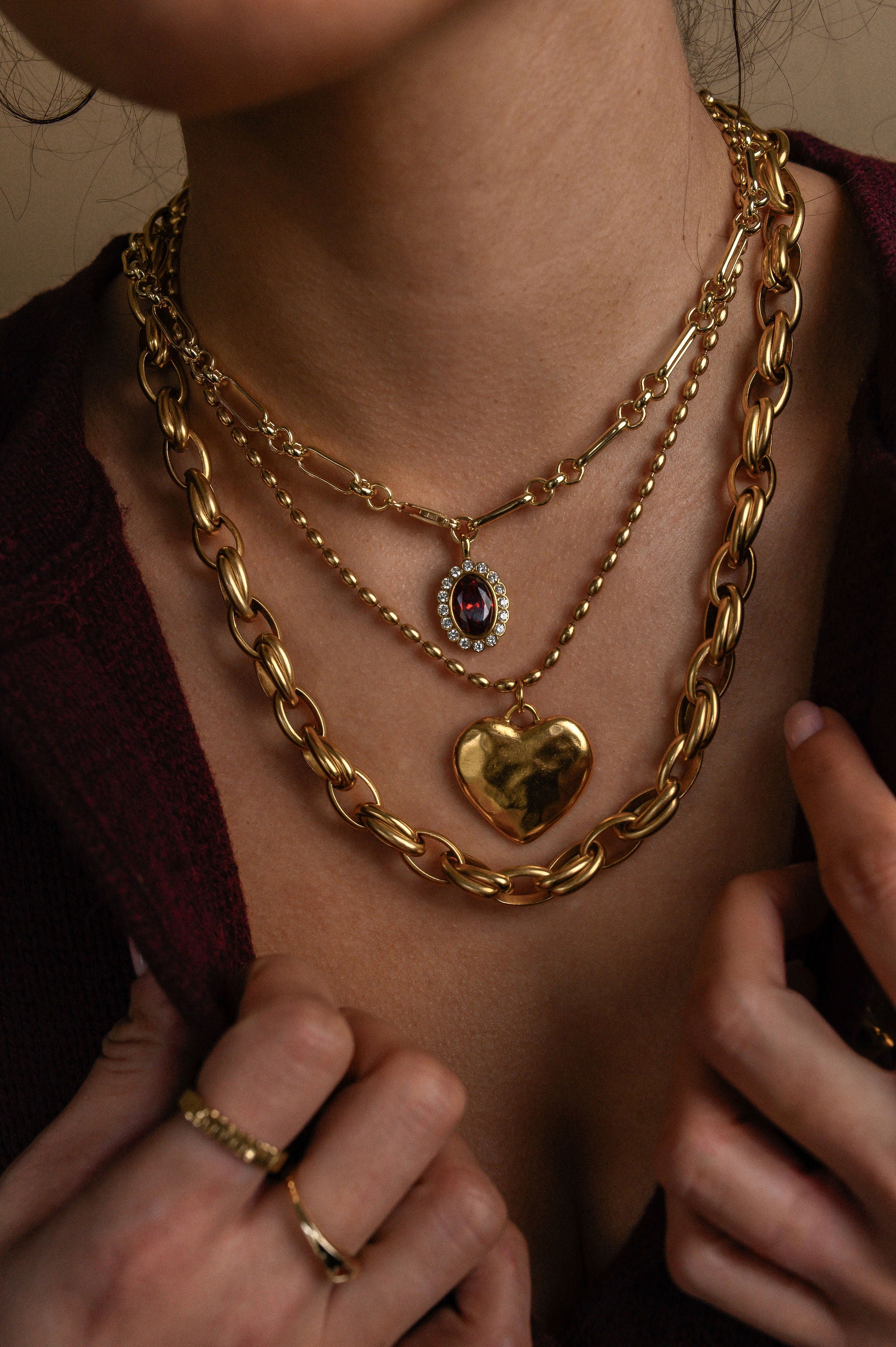 Close-up of a person wearing multiple gold necklaces with heart and chain designs.