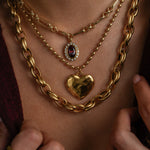 Close-up of a person wearing gold chain necklaces with heart and gemstone pendants.