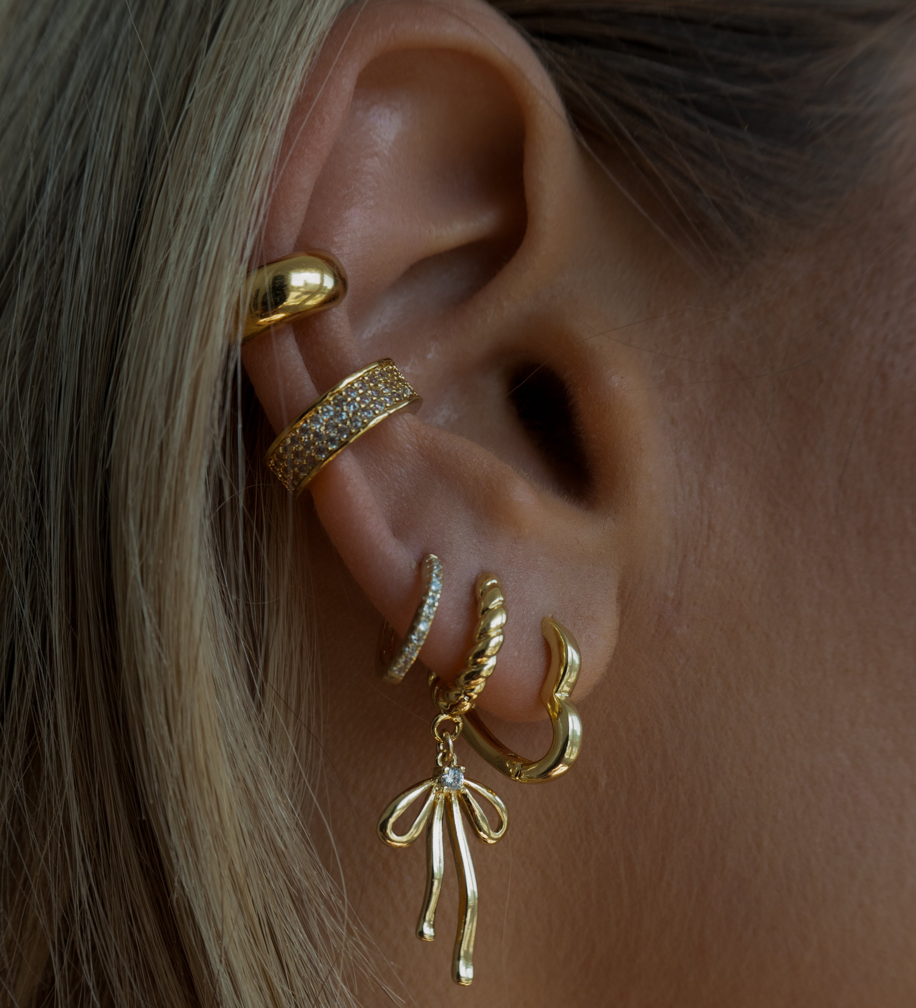 Close-up of an ear with multiple gold and crystal earrings 