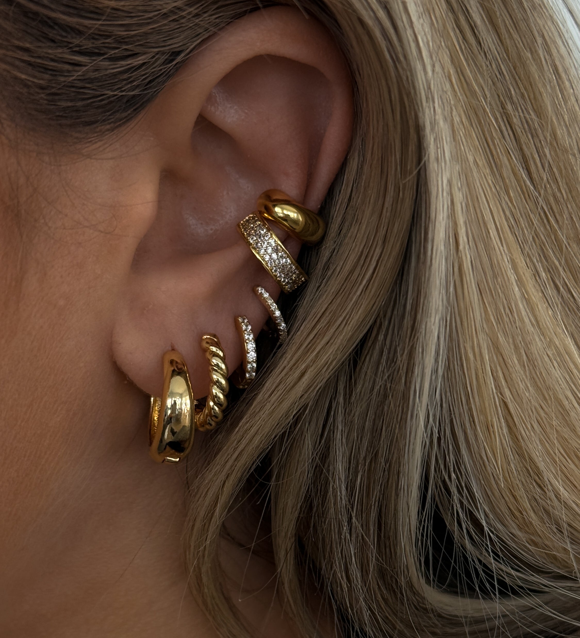 Close-up of an ear with multiple gold and crystal earrings 