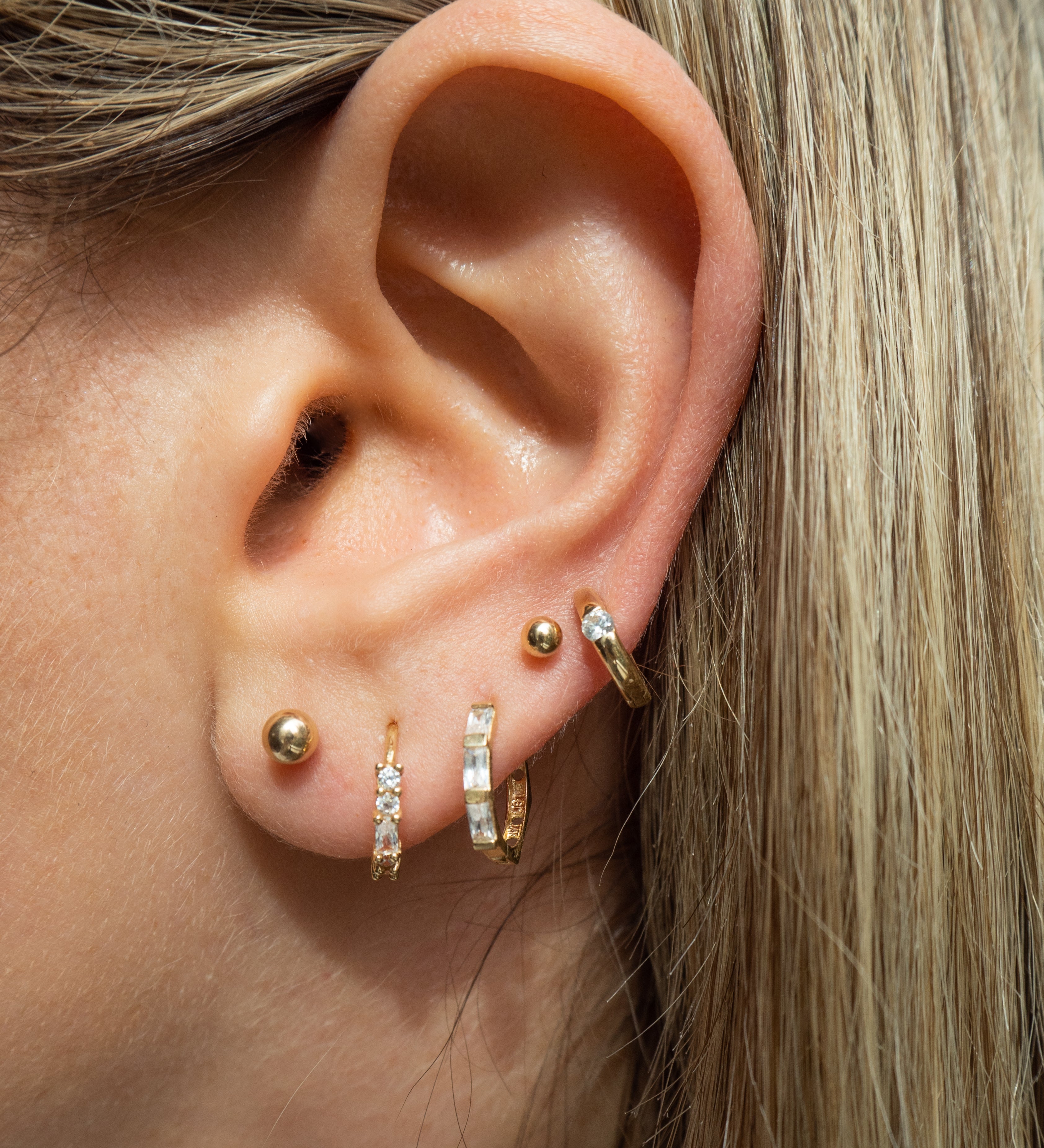 Close-up of an ear with multiple gold and crystal earrings 
