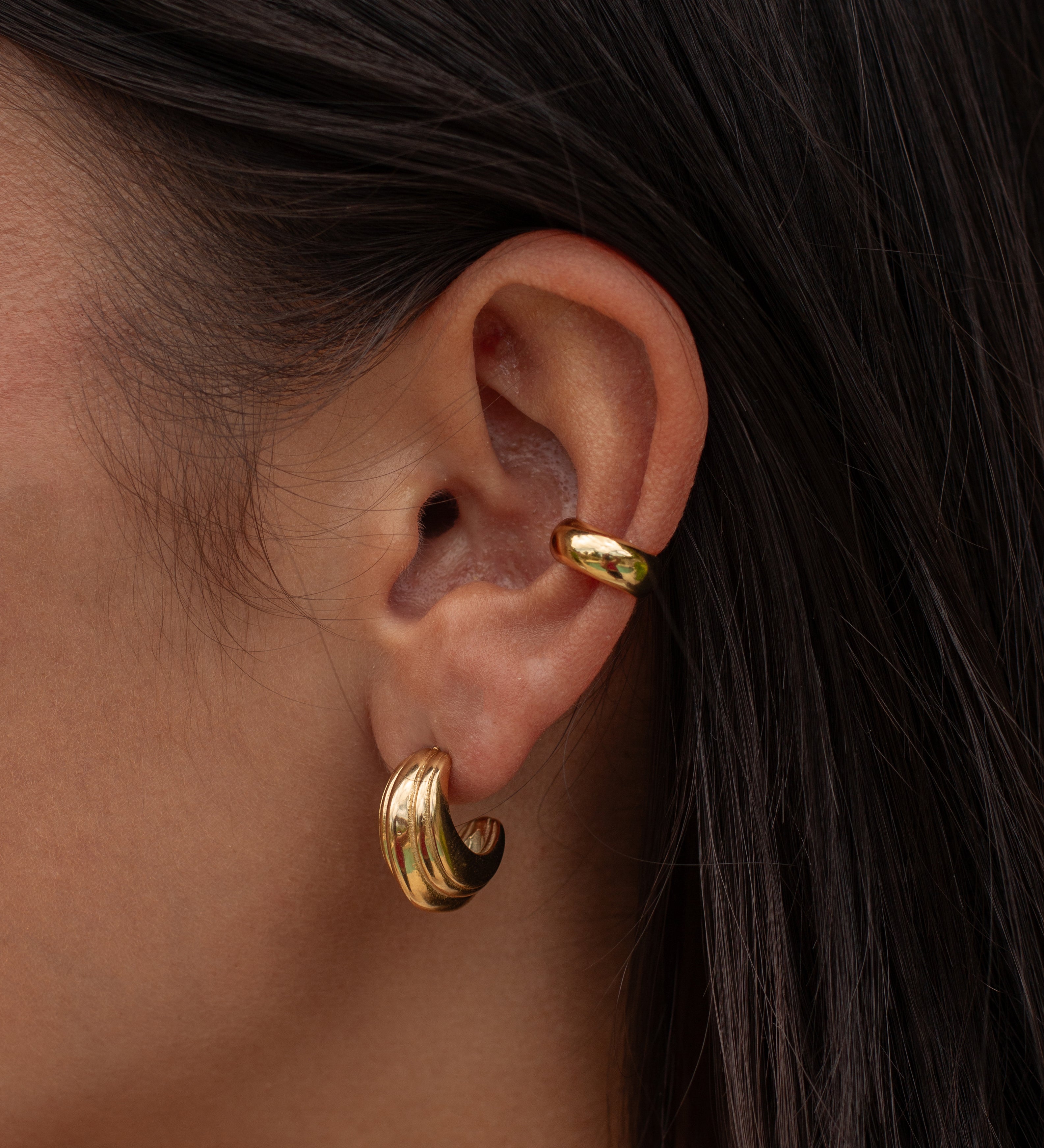 Close-up of an ear with multiple gold earrings 