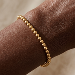 Gold beaded bracelet on a wrist with a neutral background