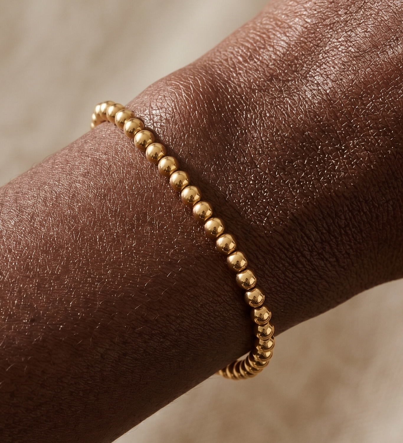 Gold beaded bracelet on a wrist with a neutral background