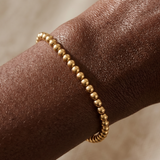 Gold beaded bracelet on a wrist with a neutral background