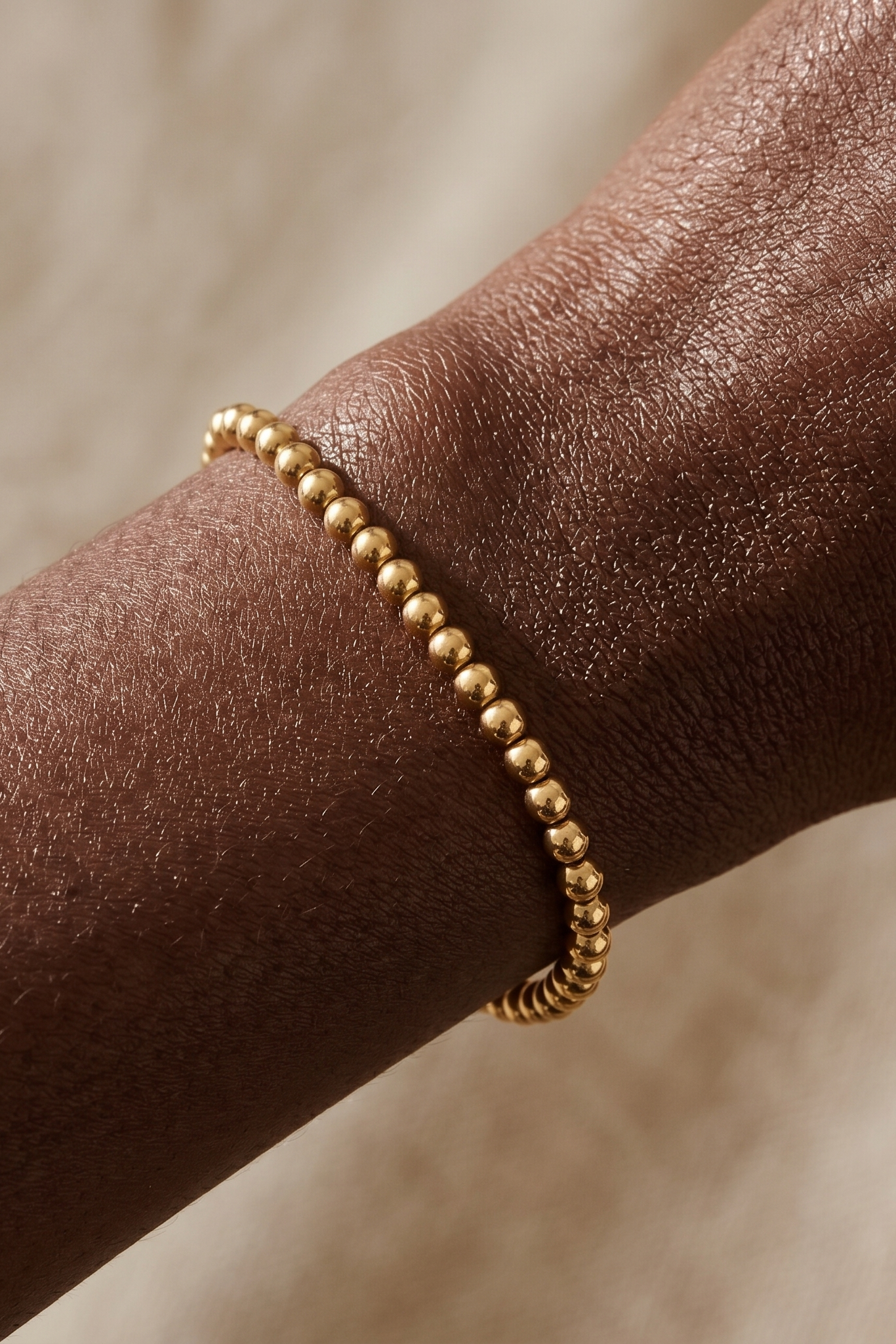 Gold beaded bracelet on a wrist with a neutral background