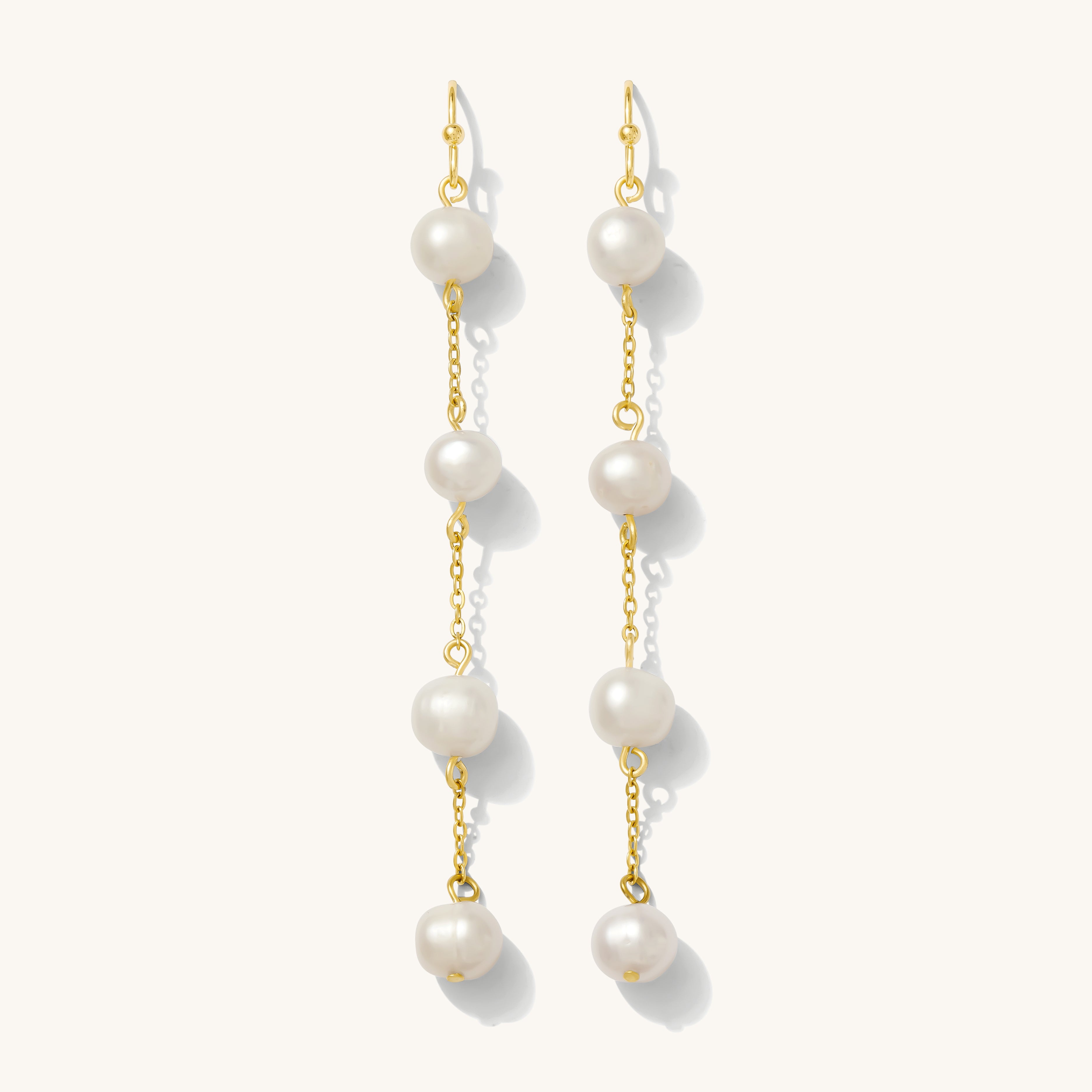 Close up of gold pearl drop earrings on a white background 