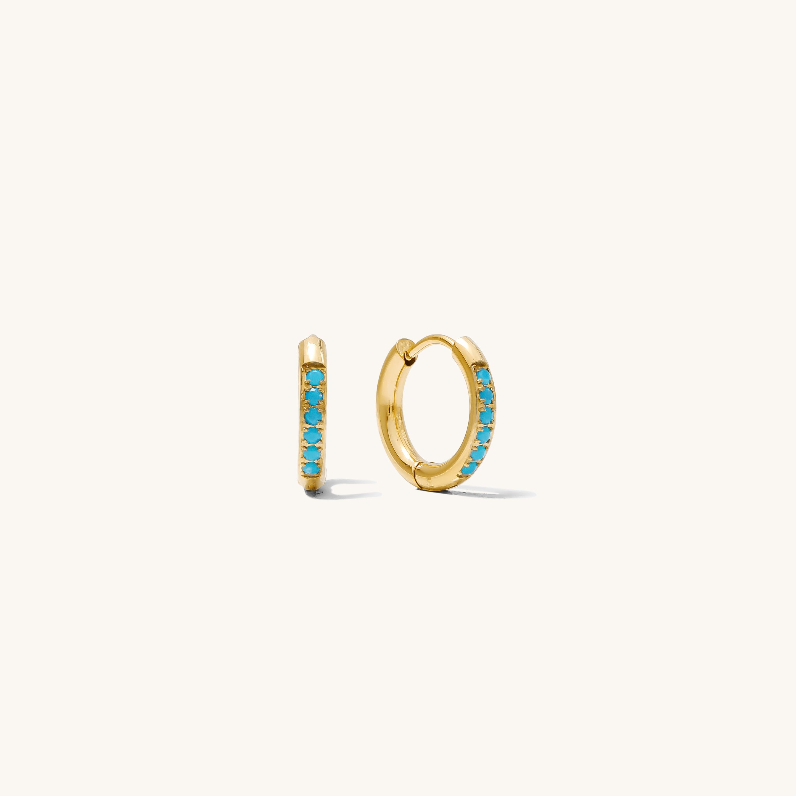 Close up of gold huggies with turquoise stones on a white background 