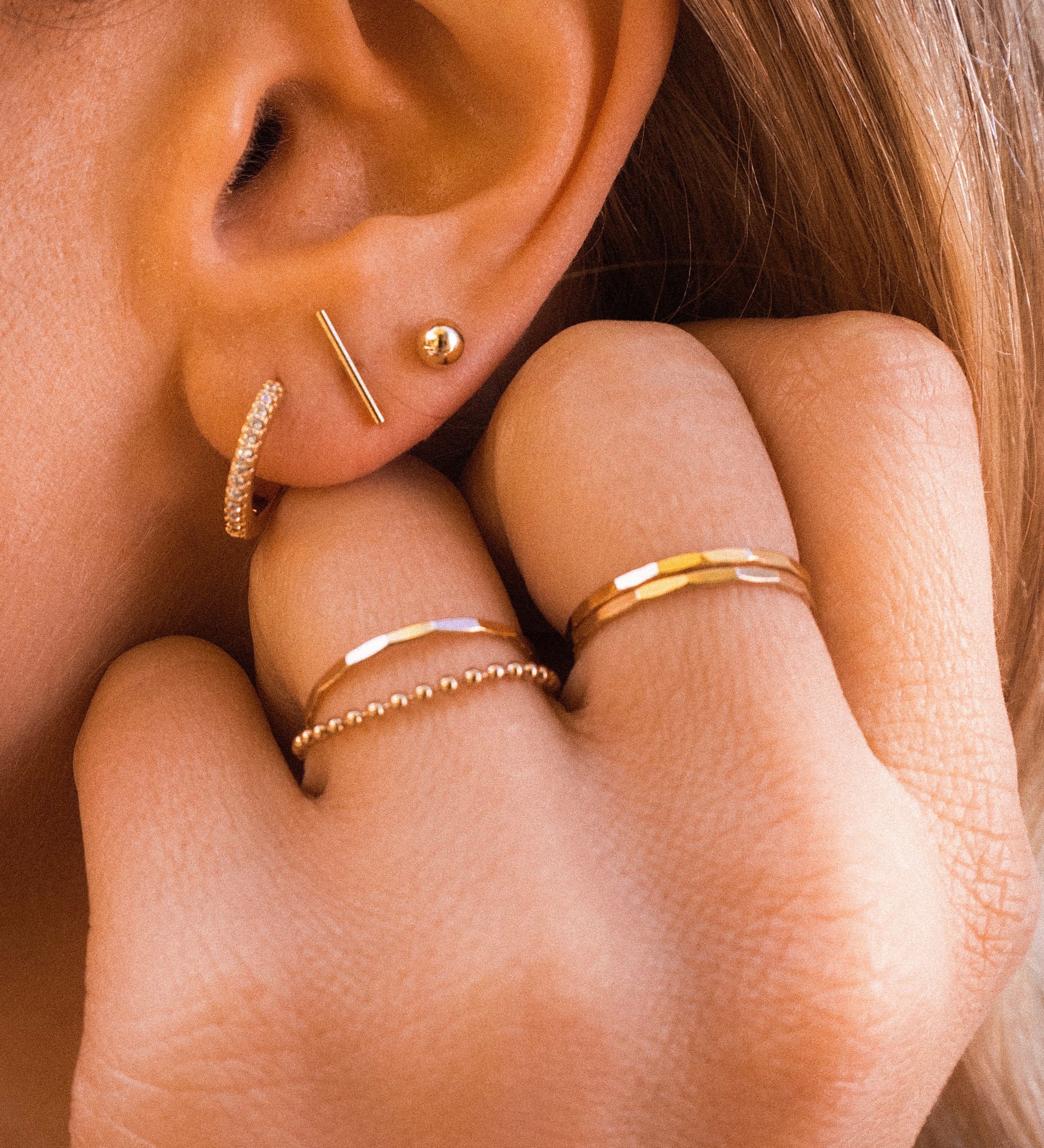 Close-up of an ear with multiple dainty gold earrings 